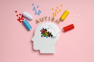 Puzzle head, word autism, threads and buttons on pink background, top view