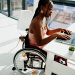 Young disabled African American woman in wheelchair at home working with laptop.